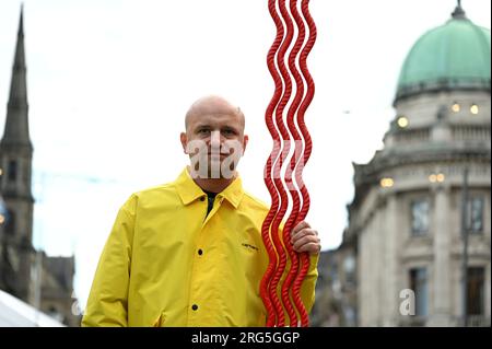 Edinburgh, Schottland, Großbritannien. 7. Aug 2023. Edinburgh Fringe: Kostya Benkovich präsentiert die rechte Hand Gottes Skulptur in den George Street Gardens, die rechte Hand Gottes vereint die traditionelle mittelalterliche Ikonographie, die diese Geste als Symbol der Gnade, Allmacht und Zuflucht darstellt. Kostya Benkovich posiert neben der Skulptur. Craig Brown/Alamy Live News Stockfoto