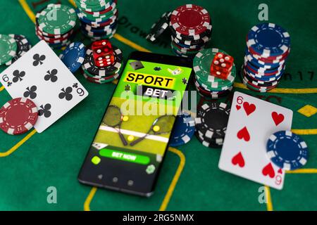 Kreativer Hintergrund, Online-Casino, in der Hand eines Mannes ein Smartphone mit Spielkarten, Roulette und Chips, schwarz-goldener Hintergrund. Internet-Glücksspiel Stockfoto