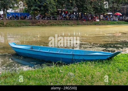 Siem Reap, Kambodscha, 22. Dezember 2018. Ein einziges blaues Boot steht am grünen Ufer eines schlammigen Flusses. Stockfoto