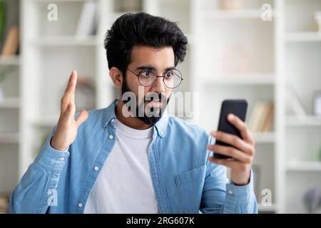 Schlechte Nachrichten. Schockierter Indianer, Der Sich Das Smartphone In Der Hand Ansieht Stockfoto