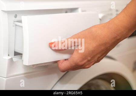 Eine Frau öffnet das Tablett, um Waschmittel in die Waschmaschine zu gießen. Das Konzept des Waschens schmutziger Wäsche in einer Waschmaschine. Verwendung von Stockfoto