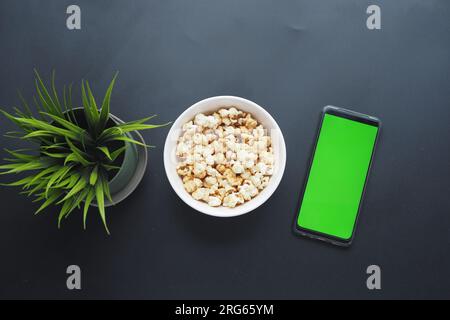 Draufsicht von Smartphone und Popcorn auf schwarzem Hintergrund Stockfoto