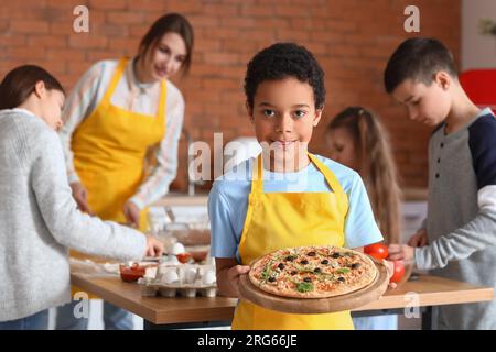 Kleiner afroamerikanischer Junge mit zubereiteter Pizza nach dem Kochkurs in der Küche Stockfoto