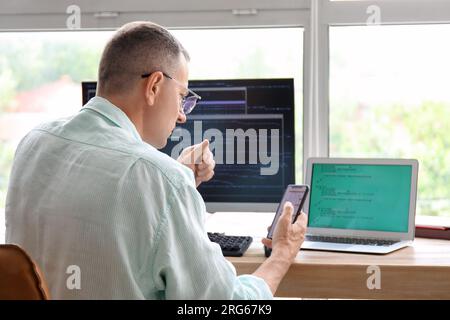 Reifer männlicher Programmierer, der an seinem Arbeitsplatz im Büro sitzt Stockfoto