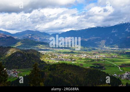 Blick auf die Stadt Bled, beleuchtet von Sonnenlicht, umgeben von Feldern und dem Karavanke-Gebirge in Gorenjska, Slowenien an einem bewölkten Tag Stockfoto