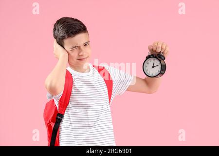 Porträt eines Schuljungen mit Rucksack mit Weckgeräusch auf pinkem Hintergrund Stockfoto
