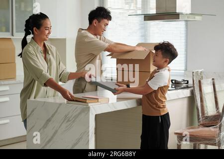 Lächelnde Frau, die ihren Sohn bittet, beim Verpacken von Büchern in Plastikkisten zu helfen Stockfoto