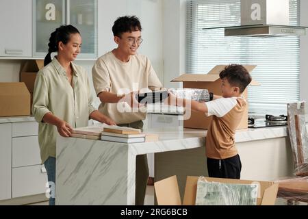 Fröhliche Eltern, die ihren Sohn bitten, verpackte Bilder in Pappkartons zu packen Stockfoto