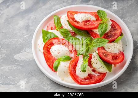 Lebhafter Caprese-Salat auf weißem Teller mit Betonhintergrund. Schließen Stockfoto