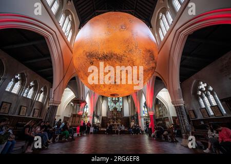 London, Großbritannien. 6. August 2023. Mars: War & Peace von Luke Jerram. Eine 7 Meter breite rotierende Nachbildung des mars von Luke Jerram, die derzeit in der All Saints' Church in Notting Hill ausgestellt wird. Die monumentale, hängende, intern beleuchtete Skulptur wurde unter Verwendung von NASA-Bildern mit 120dpi detaillierten Bildern der Marsoberfläche gebaut. Etwa eine Million Mal kleiner als der eigentliche Planet, stellt jeder Zentimeter der kugelförmigen Skulptur 10 Kilometer der Marsoberfläche dar. Kredit: Guy Corbishley/Alamy Live News Stockfoto