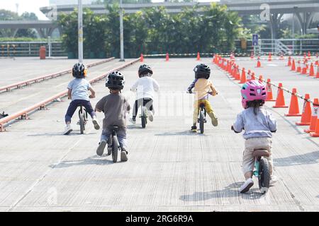 Kinder ab 2-5 Jahren fahren auf einem Balance Bike auf einem Parkplatz mit Pegeln als Strecke, Rückansicht, hinter-Sicht-Shooting. Stockfoto