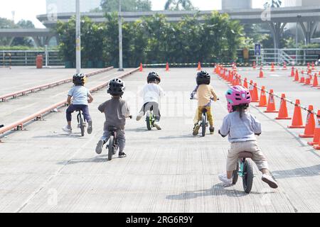 Kinder ab 2-5 Jahren fahren auf einem Balance Bike auf einem Parkplatz mit Pegeln als Strecke, Rückansicht, hinter-Sicht-Shooting. Stockfoto