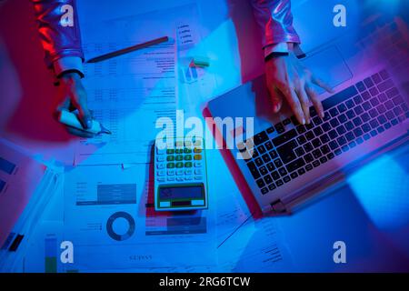 Obersicht einer modernen Frau mit Taschenrechner, Dokumenten und Laptop, die mit Karten arbeitet, in einem modernen Büro. Stockfoto