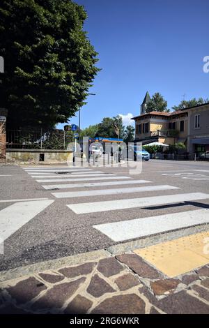 Kreuzung in einem Dorf in der italienischen Landschaft mit vorbeifahrenden Autos von einem Gehweg aus gesehen Stockfoto