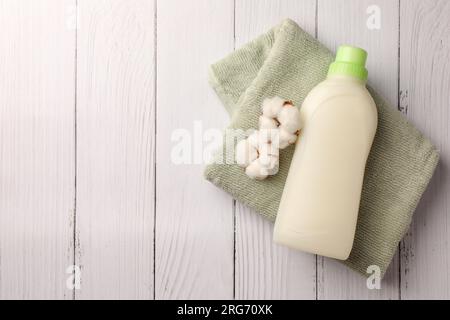 Flasche Weichspüler, Frottee-Handtuch und wunderschöne Baumwollblumen auf weißer Holzoberfläche, Draufsicht. Platz für Text Stockfoto