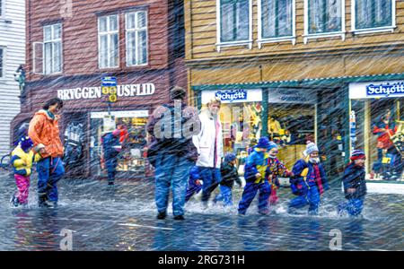 Kinder, die sich bei furchtbar schlechtem Wetter auf den überfluteten Straßen in Bryggen in Bergen, Norwegen, amüsieren. Stockfoto