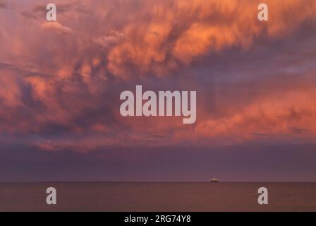 Stürmt Wolken über dem Ozean während der goldenen Stunde mit Bohrwagen am Horizont Stockfoto
