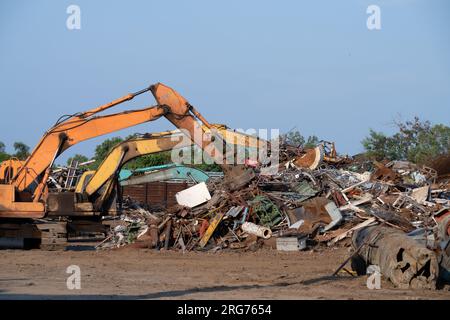 Magnet des Hydraulikbaggers hebt Stahlschrott aus dem Recyclingmaterialhaufen auf dem Schrottplatz in der Recyclingfabrik. Bagger mit Elektro- und Magnetsauger Stockfoto