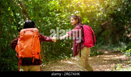 Zwei Wanderer mit Rucksäcken wandern durch den Wald und genießen die Aussicht auf das Tal und machen Fotos. Helft euch gegenseitig Stockfoto
