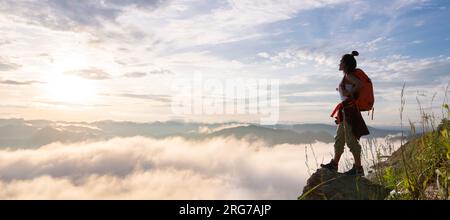 Eine Wanderin steht und beobachtet das Meer von ​​mist auf einem hohen Berg. Erfolgreiche Bergsteiger Stockfoto