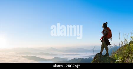 Eine Wanderin steht und beobachtet das Meer von ​​mist auf einem hohen Berg. Erfolgreiche Bergsteiger Stockfoto