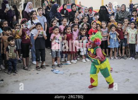 Gaza-Stadt, Palästina. 07. Aug. 2023. Ein als Clown verkleideter palästinensischer Mann führt im Flüchtlingslager Jabalia im nördlichen Gazastreifen unter den hohen Temperaturen und Stromausfällen während der andauernden israelischen Blockade Unterhaltungsaktivitäten für Kinder durch. Für die Palästinenser, die im überfüllten Gazastreifen leben, wurde die schwelende Sommerhitze durch die durch die anhaltende israelische Blockade verursachten Stromausfälle noch verschärft. Kredit: SOPA Images Limited/Alamy Live News Stockfoto