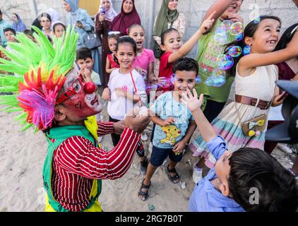 Gaza-Stadt, Palästina. 07. Aug. 2023. Ein als Clown verkleideter palästinensischer Mann führt im Flüchtlingslager Jabalia im nördlichen Gazastreifen unter den hohen Temperaturen und Stromausfällen während der andauernden israelischen Blockade Unterhaltungsaktivitäten für Kinder durch. Für die Palästinenser, die im überfüllten Gazastreifen leben, wurde die schwelende Sommerhitze durch die durch die anhaltende israelische Blockade verursachten Stromausfälle noch verschärft. Kredit: SOPA Images Limited/Alamy Live News Stockfoto