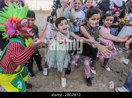 Gaza-Stadt, Palästina. 07. Aug. 2023. Ein als Clown verkleideter palästinensischer Mann führt im Flüchtlingslager Jabalia im nördlichen Gazastreifen unter den hohen Temperaturen und Stromausfällen während der andauernden israelischen Blockade Unterhaltungsaktivitäten für Kinder durch. Für die Palästinenser, die im überfüllten Gazastreifen leben, wurde die schwelende Sommerhitze durch die durch die anhaltende israelische Blockade verursachten Stromausfälle noch verschärft. Kredit: SOPA Images Limited/Alamy Live News Stockfoto