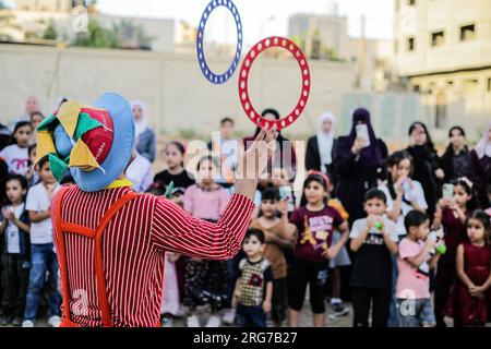 Gaza-Stadt, Palästina. 07. Aug. 2023. Ein als Clown verkleideter palästinensischer Mann führt im Flüchtlingslager Jabalia im nördlichen Gazastreifen unter den hohen Temperaturen und Stromausfällen während der andauernden israelischen Blockade Unterhaltungsaktivitäten für Kinder durch. Für die Palästinenser, die im überfüllten Gazastreifen leben, wurde die schwelende Sommerhitze durch die durch die anhaltende israelische Blockade verursachten Stromausfälle noch verschärft. Kredit: SOPA Images Limited/Alamy Live News Stockfoto