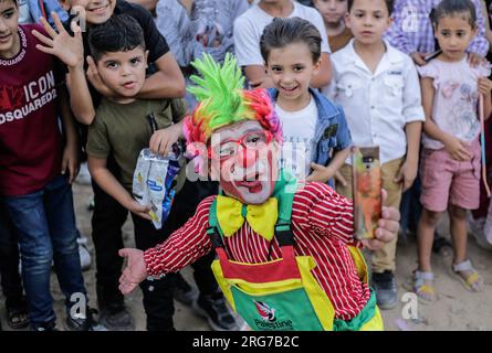 Gaza-Stadt, Palästina. 07. Aug. 2023. Ein als Clown verkleideter palästinensischer Mann führt im Flüchtlingslager Jabalia im nördlichen Gazastreifen unter den hohen Temperaturen und Stromausfällen während der andauernden israelischen Blockade Unterhaltungsaktivitäten für Kinder durch. Für die Palästinenser, die im überfüllten Gazastreifen leben, wurde die schwelende Sommerhitze durch die durch die anhaltende israelische Blockade verursachten Stromausfälle noch verschärft. Kredit: SOPA Images Limited/Alamy Live News Stockfoto