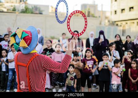 Gaza-Stadt, Palästina. 07. Aug. 2023. Ein als Clown verkleideter palästinensischer Mann führt im Flüchtlingslager Jabalia im nördlichen Gazastreifen unter den hohen Temperaturen und Stromausfällen während der andauernden israelischen Blockade Unterhaltungsaktivitäten für Kinder durch. Für die Palästinenser, die im überfüllten Gazastreifen leben, wurde die schwelende Sommerhitze durch die durch die anhaltende israelische Blockade verursachten Stromausfälle noch verschärft. (Foto: Mahmoud Issa/SOPA Images/Sipa USA) Guthaben: SIPA USA/Alamy Live News Stockfoto