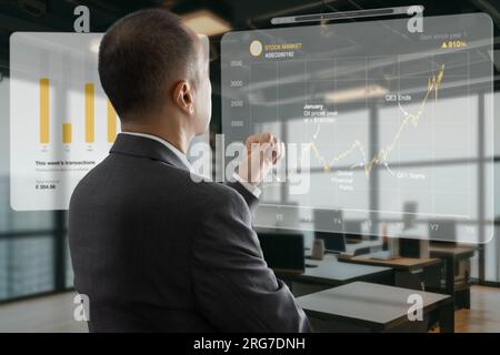 Asiatischer Geschäftsmann im Büro, der mit Augmented Reality oder virtuellem Touchscreen interagiert, um Diagramme für die Analyse von Geschäftsdaten zu prüfen Stockfoto