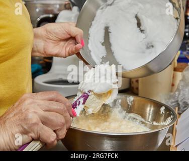 Der Koch gibt dem Kuchenteig in der Schüssel Eiweiß hinzu Stockfoto