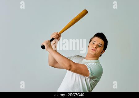 Ein Mann mit einem Schläger in der Hand schwingt auf grauem Hintergrund Stockfoto
