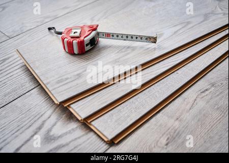 Maßband auf Holzböden für Hausrenovierungs-, Bauarbeiten- und Innenausbau. Metallbandmaß an Proben von Laminatplatten mit Muster und Holzstruktur für Bodenbeläge. Stockfoto