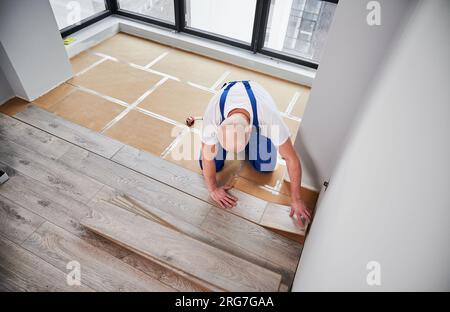 Draufsicht eines Bauarbeiters, der Laminatfußböden im Wohnzimmer verlegt. Mann legt Laminat-Holzbohle auf Bodenunterlage in neuer Wohnung. Hausrenovierungskonzept. Stockfoto