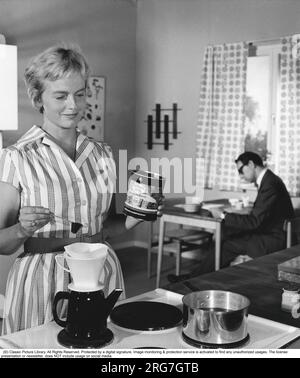 Kaffee in den 1960er. Eine Frau macht Kaffee für sich und ihren Mann. Die Art und Weise, Kaffee zu dieser Zeit zuzubereiten, bestand in der Regel darin, heißes Wasser durch einen Filterhalter in eine Kaffeekanne zu gießen. Es gab bereits im 19. Jahrhundert elektrische Kaffeemaschinen, aber die moderne elektrische Maschine, wie wir sie heute kennen, wurde erst in den 1950er Jahren auf den Markt gebracht. Melitta hat in den 1960er Jahren die erste Kaffeemaschine „MA 120“ auf den Markt gebracht. Zu dieser Zeit war ein Elektromacher ein echtes Luxusobjekt. Heute ist die elektrische Kaffeemaschine eher ein Standardprodukt, das in fast jedem Zuhause zu finden ist, und es gibt eine ganze Menge Kaffee ma Stockfoto