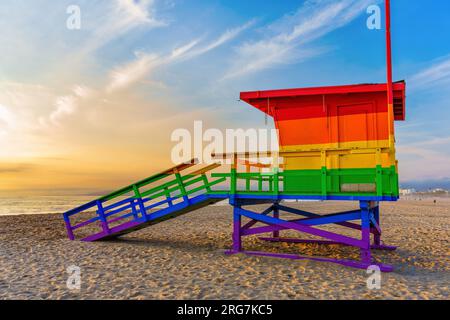 Der regenbogenfarbene Rettungsschwimmturm vor dem Hintergrund des schimmernden Ozeans und eines atemberaubenden Sonnenuntergangs. Stockfoto