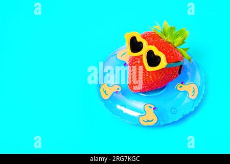 Saftige Erdbeeren, geschmückt mit stilvoller Sonnenbrille, genießen ein entspannendes Sonnenbaden, während sie anmutig in einem Poolring schwimmt. Sommerurlaub CO Stockfoto