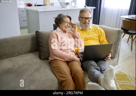 Ältere Paare, die zusammen ein Notebook benutzen und zu Hause auf dem Sofa sitzen Stockfoto