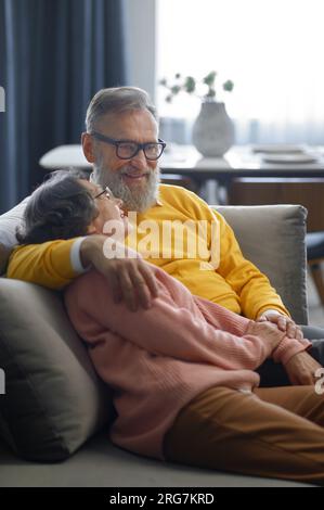 Glückliches, liebevolles Seniorenpaar, das sich zu Hause auf dem Sofa umarmt Stockfoto