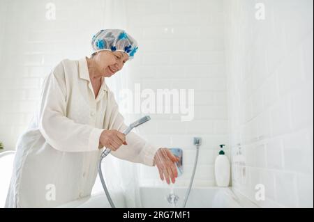 Ältere Frau im Bademantel, die die Badewanne mit Wasser füllt Stockfoto