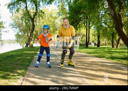 Glücklicher Seniorenmann und kleiner Junge beim Rollschuhlaufen im Stadtpark Stockfoto