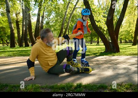 Ein kleiner Junge, der dem alten Großvater Rollschuhlaufen beibringt Stockfoto