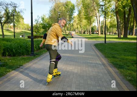 Ein älterer Mann, der Rollschuhe fährt und zurück in die Kamera schaut Stockfoto