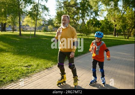 Glücklicher Seniorenmann und kleiner Junge beim Rollschuhlaufen im Stadtpark Stockfoto