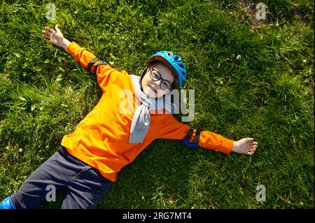 Fröhlicher, müder Junge mit Rollschuhen und Helm auf grünem Gras Stockfoto