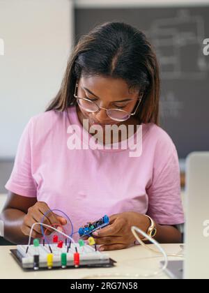 Eine afroamerikanische Studentin, die im Technologiekurs mit elektronischen Schaltungen experimentiert Stockfoto