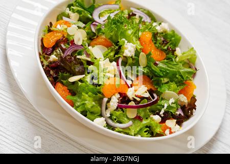 Mandarin-Orangensalat mit Salatmischung, gerösteten Mandeln, getrockneten Cranberries, roten Zwiebeln und Fetakäse in weißer Schüssel, Nahaufnahme Stockfoto