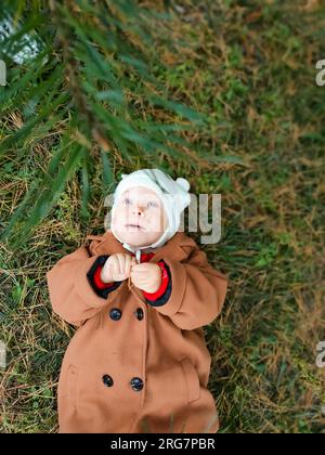 Ein kleines Kind liegt auf dem Boden und lächelt. Draufsicht. Das Konzept der Herbstblätter für Kinder. Ein Lächeln im Gesicht eines Kindes. Ein kleines Kind in einem Stockfoto